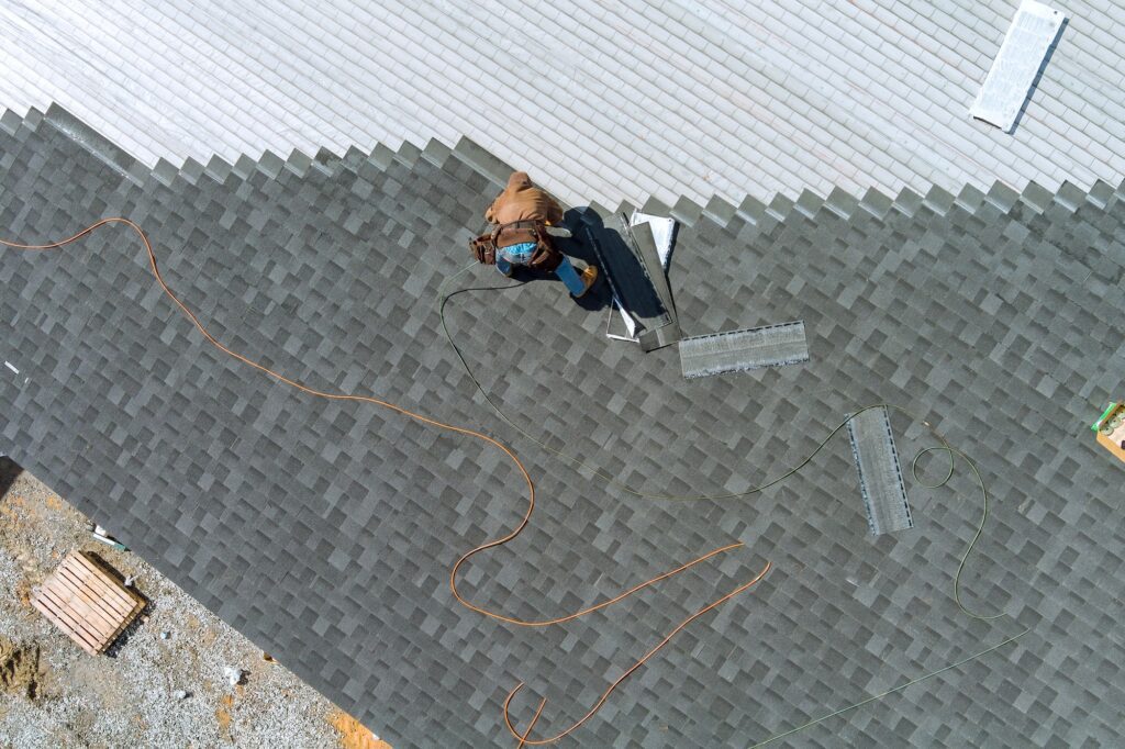 A asphalt shingles installation on the roof roofer is nailing asphalt shingles to roofing constructi